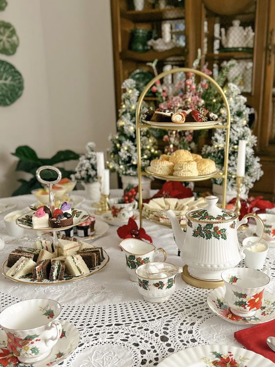 an elegant Christmas tea party table with a tablecloth, tiered stands with sweets and cookies, printed teaware and candles and evergreens