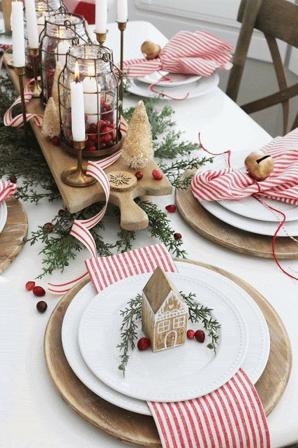 an eye catchy Christmas tea party table with a centerpiece of candles and candle lanterns with cranberries, wooden placemats, plates with bells and gingerbread houses