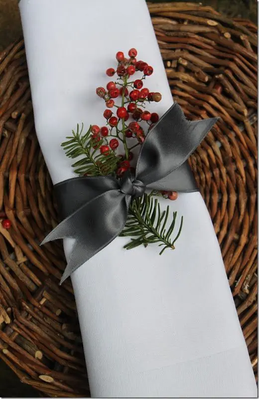 a napkin topper with holly and evergreens, an elgant bow