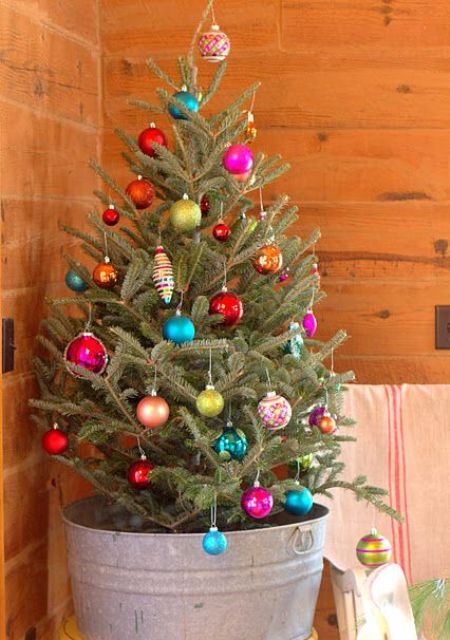 a small natural tree in a bucket decorated with colorful ornaments looks unusual