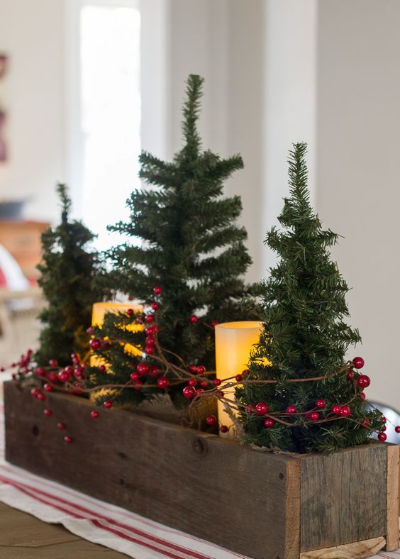 a wooden planter with small trees, candles and holly berries