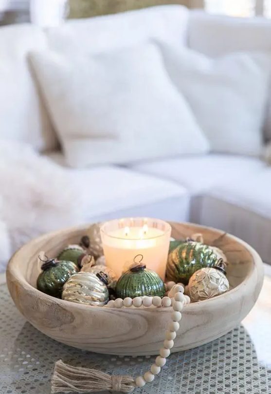 a Scandi Christmas arrangement of a wooden bowl with green and gold ornaments, a candle and wooden beads plus a tassel