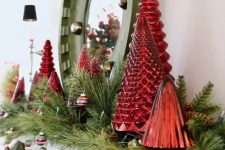 a bold Christmas mantel decorated with evergreens, vintage ornaments, red mercury glass Christmas trees and a mirror in a green frame