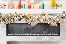 a bold Christmas mantel with colorful bottle brush Christmas trees, a snowy evergreen garland with lights