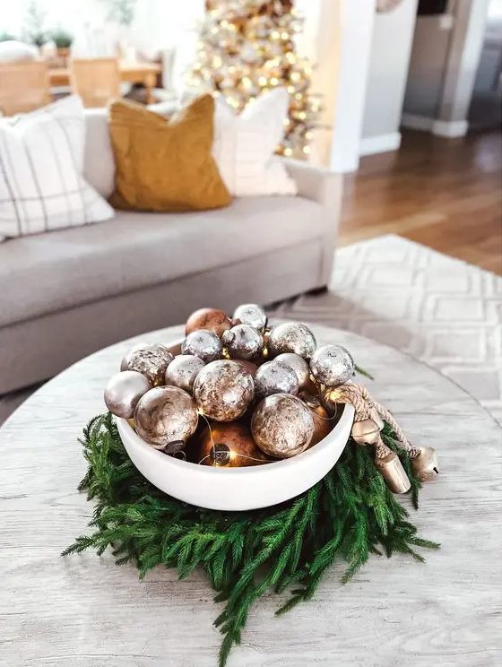a bowl surrounded with evergreens, with copper and silver ornaments and lights plus bells is a catchy and cool idea