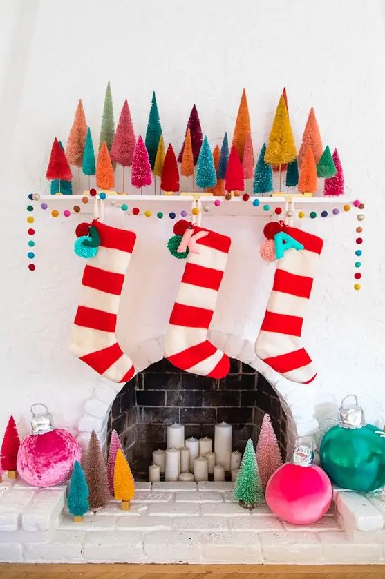 a colorful Christmas mantel with super bold bottle cleaner Christmas trees, a colorful pompom garland and stockings plus oversized ornaments around