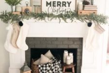 a farmhouse Christmas fireplace with evergreens, mini trees, a sgin, some stockings and a plaid blanket