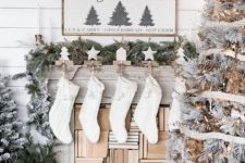a farmhouse Christmas living room with a snowy Christmas tree with lights, knit stockings, mini trees and signs over the mantel