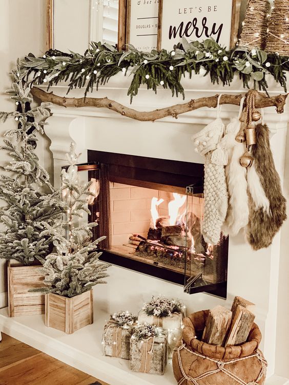 a farmhouse Christmas mantel with a greenery and pompom garland, flocked Christmas trees, gifts and firewood