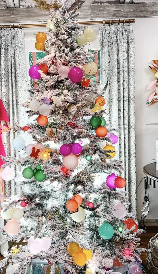 a flocked Christmas tree with bold ornaments and lights is a cool and chic decoration you'll like