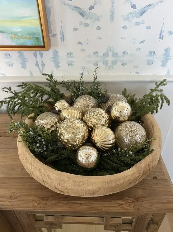 a glam Christmas arrangement of a wooden bowl with evergreens and gold ornaments is a lovely idea