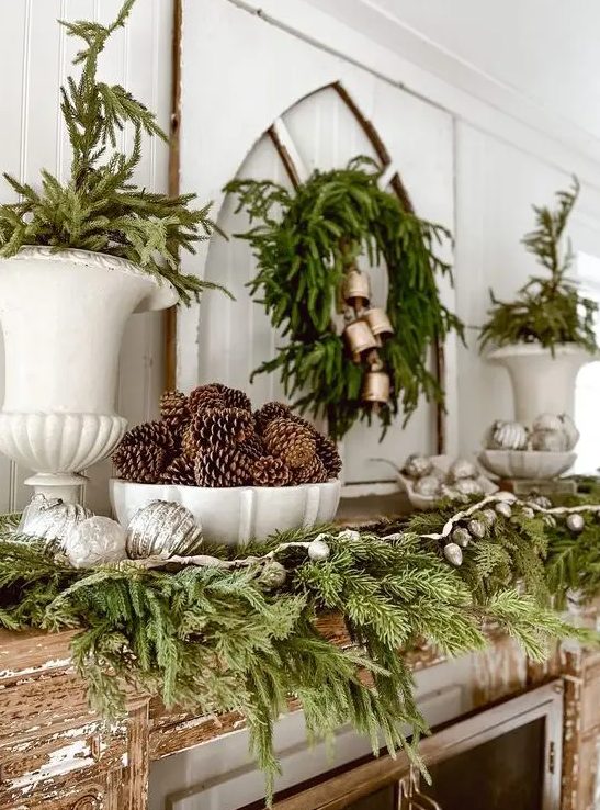 a gorgeous woodland Christmas mantel with evergreens, pinecones, lights, ornaments and bells is awesome