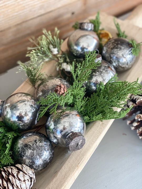 a holiday arrangement of a dough bowl, evergreens, pinecones and mercury glass ornaments is a lovely idea