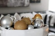 a large soup bowl filled with silver, gold and gold glitter ornaments for Christmas