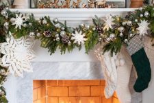 a lovely winter wonderland Christmas mantel with an evergreen garland, ornaments, pinecones, stockings and mini deer