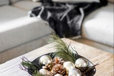a modern Christmas centerpiece of a black bow, evergreens, twigs, silver ornaments and snowy pinecones