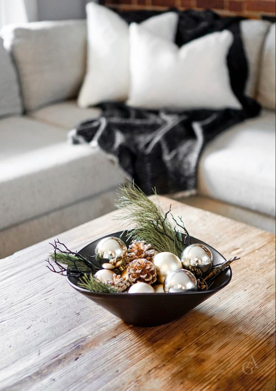a modern Christmas centerpiece of a black bow, evergreens, twigs, silver ornaments and snowy pinecones