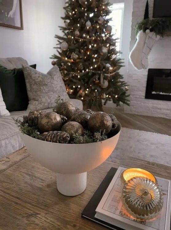a modern Christmas centerpiece of a white bowl with evergreens, pinecones, brown ornaments is a cool solution