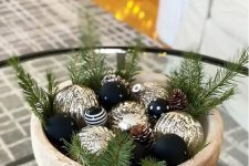 a modern glam Christmas centerpiece of a wooden bowl with black and gold ornaments, evergreens is a lovely idea