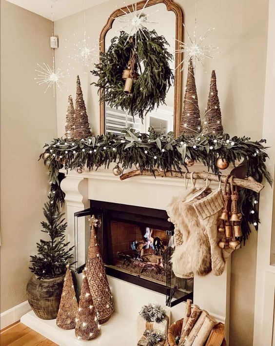 a pretty Christmas mantel with evergreens, pompoms, twine cone trees, stockings, bells and a tree in a pot