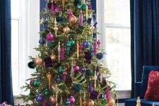 a refined and bold jewel-tone Christmas tree with pink, navy, green, gold and purple ornaments, gold icicles and bold lights