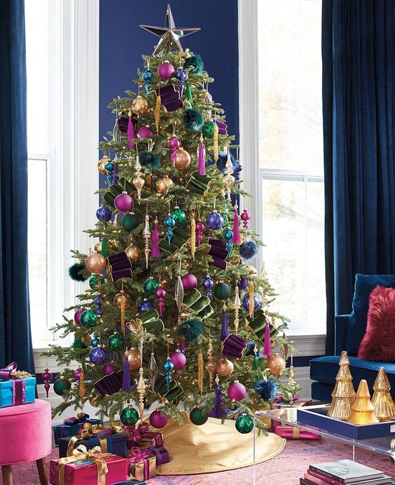 A refined and bold jewel tone Christmas tree with pink, navy, green, gold and purple ornaments, gold icicles and bold lights