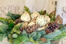 a rustic Christmas centerpiece of a wooden bowl, evergreens, pinecones and artichokes is a cozy rustic decor idea