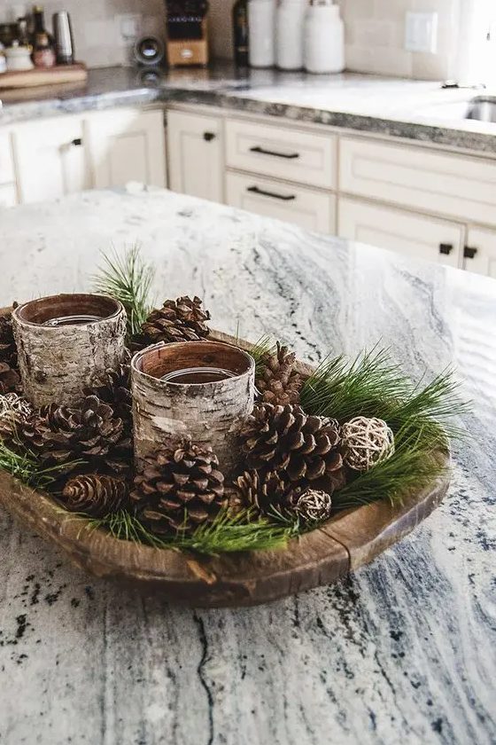 a rustic Christmas centerpiece of a wooden bowl with evergreens, pinecones and candles wrapped with bark