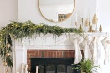a simple and natural Christmas mantel with an evergreen garland, lights, bottlebrush trees and candles