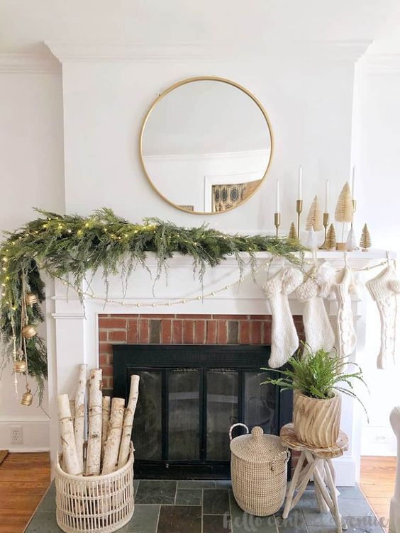 a simple and natural Christmas mantel with an evergreen garland, lights, bottlebrush trees and candles