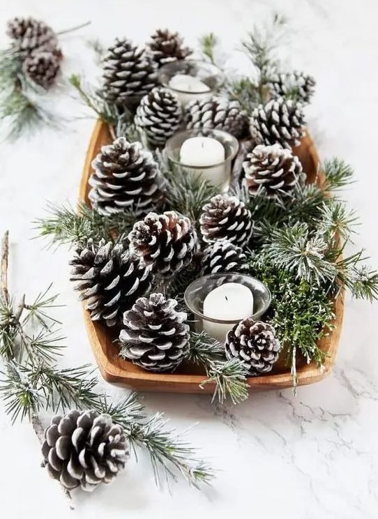 a simple and natural centerpiece of a dough bowl, snowy pinecones and evergreens and several candles for holidays