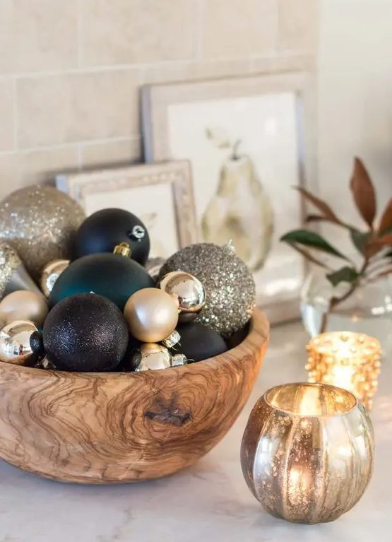 a simple glam Christmas centerpiece of a wooden bowl with gold, black and dark green ornaments of various sizes