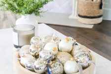 a simple modern Christmas centerpiece of a wooden bowl with white and mercury glass ornaments