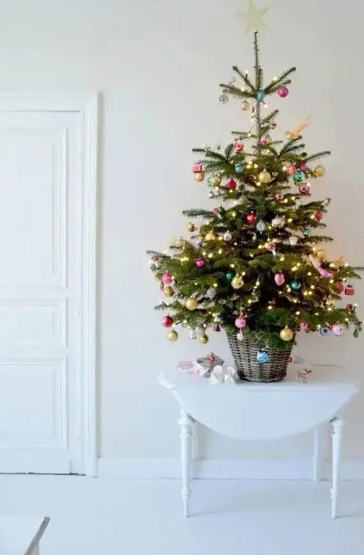 a tabletop Christmas tree in a basket, with lights and colorful ornaments is an adorable decoration for any space