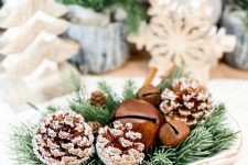 a small holiday arrangement of a wooden bowl, evergreens, snowy pinecones and bells is a lovely centerpiece