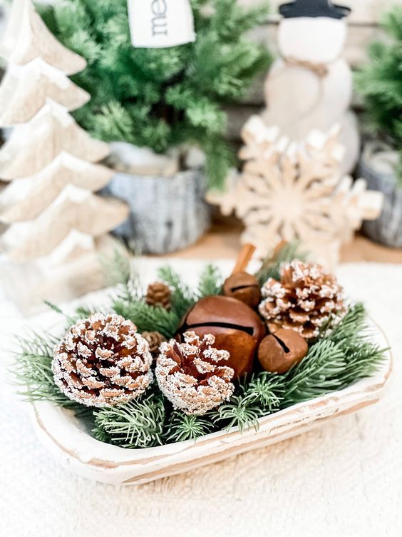 a small holiday arrangement of a wooden bowl, evergreens, snowy pinecones and bells is a lovely centerpiece