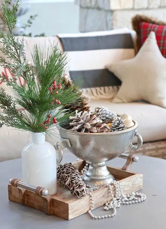 a small metal bowl with ornaments and snowy pinecones is a cool decor idea with an elegant feel