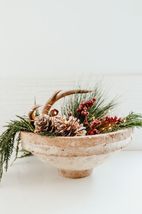 a stone bowl with evergreens, faux berries, pinecones and antlers plus lights is a cool Christmas centerpiece