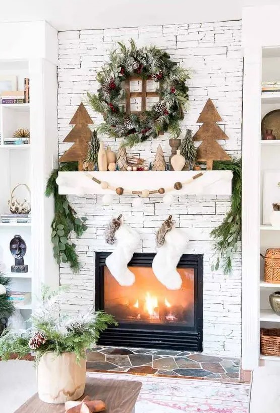 a stylish Scandi Christmas mantel with wooden trees, vases, a wooden bead garland, an evergreen and pinecone wreath plus stockings