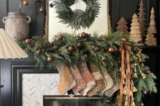 a stylish holiday mantel with vintage stockings, a lush evergreen garland with chocolate brown ornaments and bells, Christmas trees