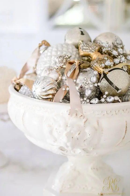 a vintage white bowl with silver and gold ornaments and bells plus ribbon is a cool centerpiece for the holidays