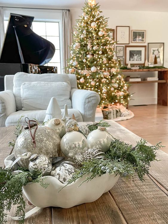 a white porcelain bowl with evergreens, creamy and silver ornaments and berries is a cool Christmas centerpiece