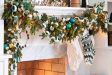 a winter wonderland Christmas mantel with a lush evergreen garland with ornaments, mini trees and a lantern