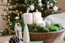 a wooden Christmas centerpiece of a wooden bowl with moss and pillar candles is a lovely idea