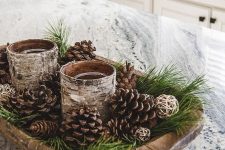 a woodland Christmas centerpiece of a dough bowl, evergreens, pinecones, candle glasses wrapped with bark