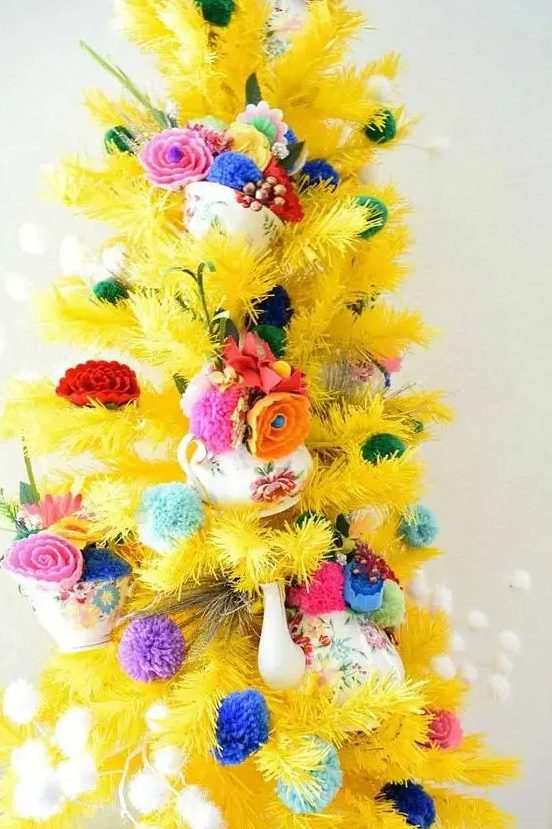 a yellow Christmas tree styled with colorful pompoms, bold fabric blooms and beads is a whimsical and catchy idea
