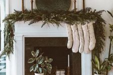 an all-natural Christmas mantel with a super lush evergreen and fern garland with pinecones, tall and thin candles, neutral stockings