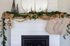 an all-natural Christmas mantel with an evergreen garland, a dried citrus garland and pompoms, burlap stockings and oversized bells