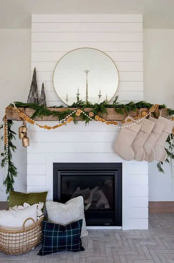 An all natural Christmas mantel with an evergreen garland, a dried citrus garland and pompoms, burlap stockings and oversized bells