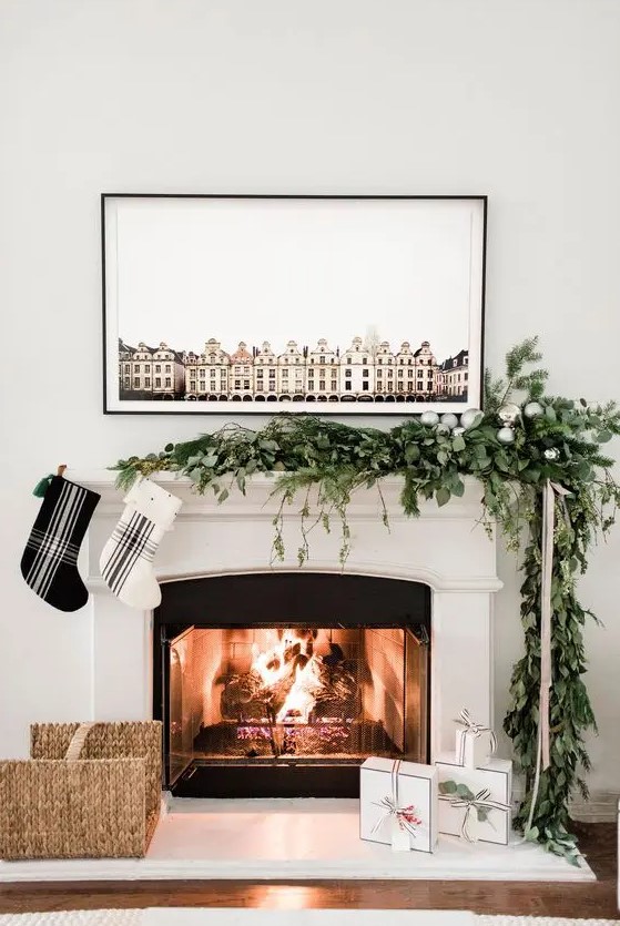 An ultra modern Christmas mantel with a greenery and evergreen garland with silver ornaments, and a duo of black and white plaid stockings